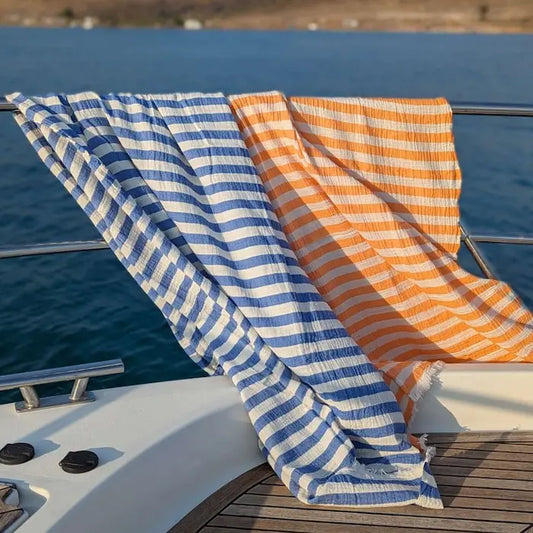 Blue and orange striped Summer Forever cotton beach towels on a boat deck with ocean in the background