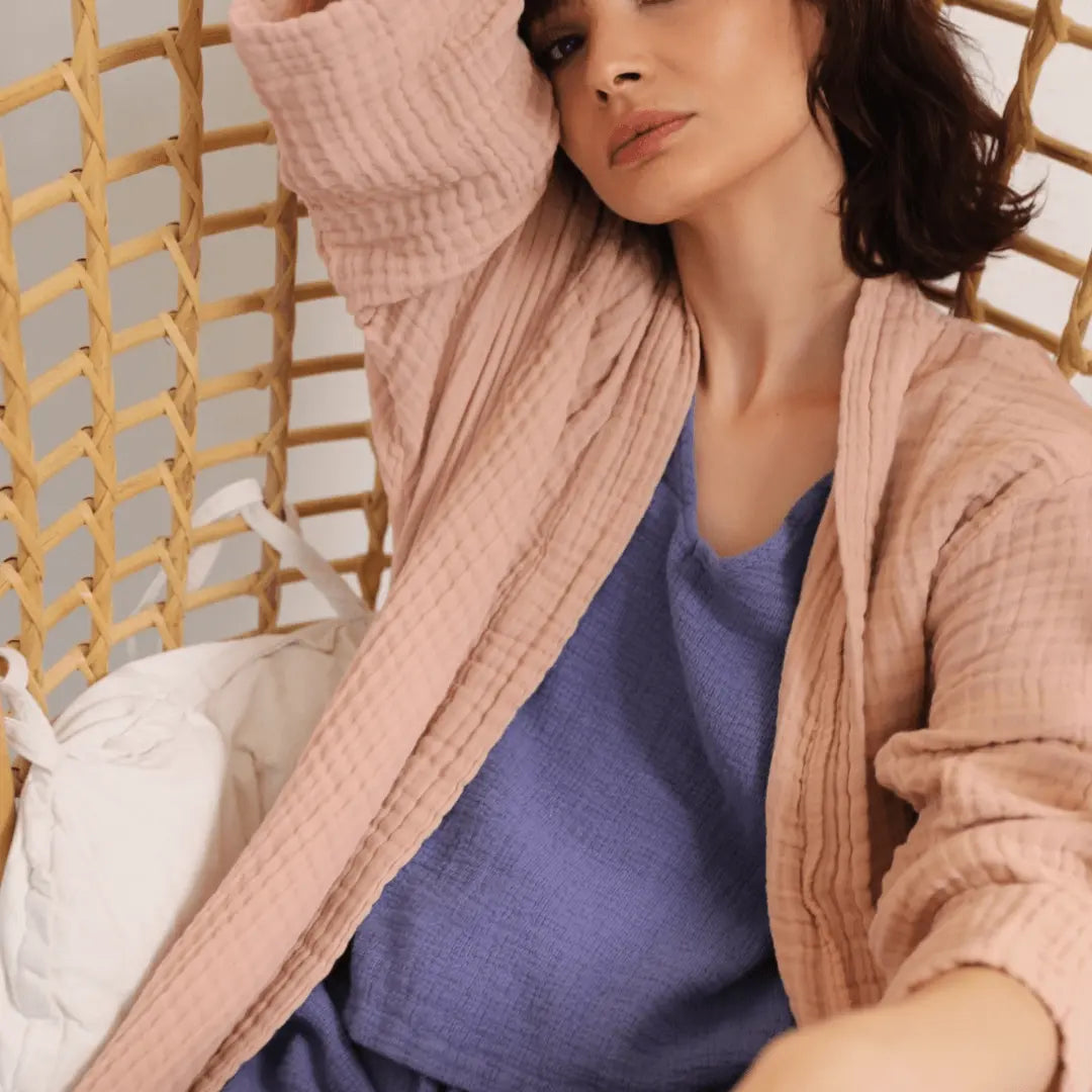Woman wearing a pink muslin cotton Summer Forever robe relaxing on a chair
