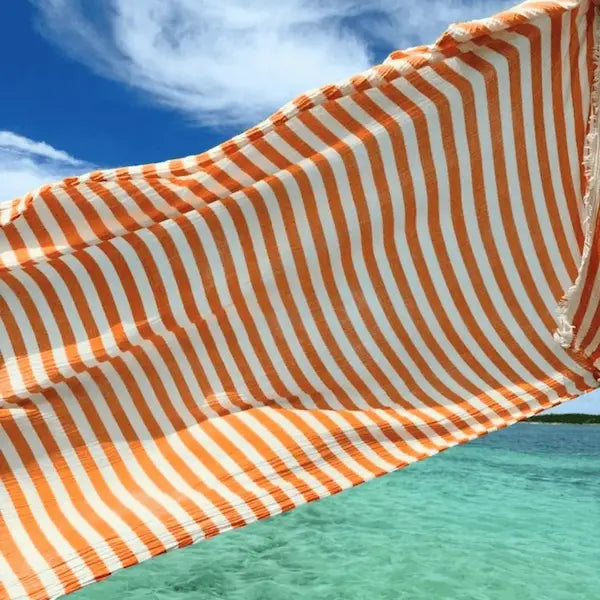 Orange and white striped fabric draped over a blue sky and turquoise water.