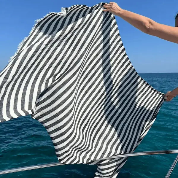 Person holding an extra large black and white Summer Forever striped cotton beach towel  towel over the ocean and sky