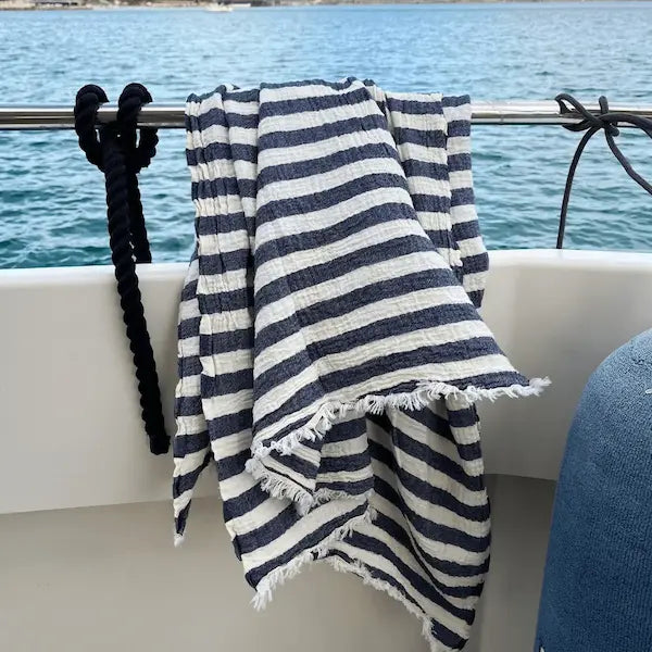 Navy and white striped Summer Forever  cotton beach towel  draped over a railing with lake in the background