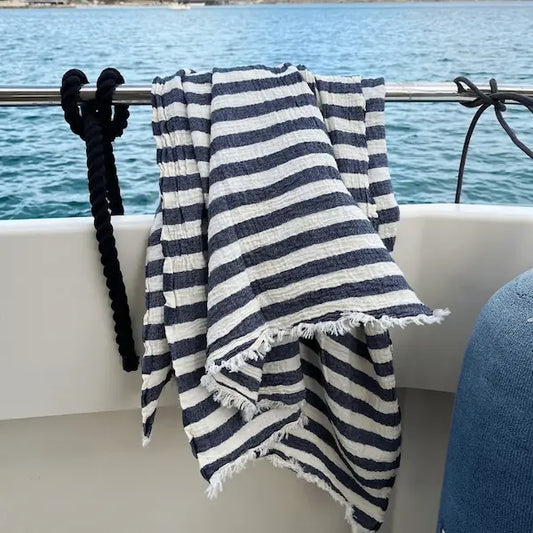 Navy and white striped Summer Forever  cotton beach towel  draped over a railing with lake in the background